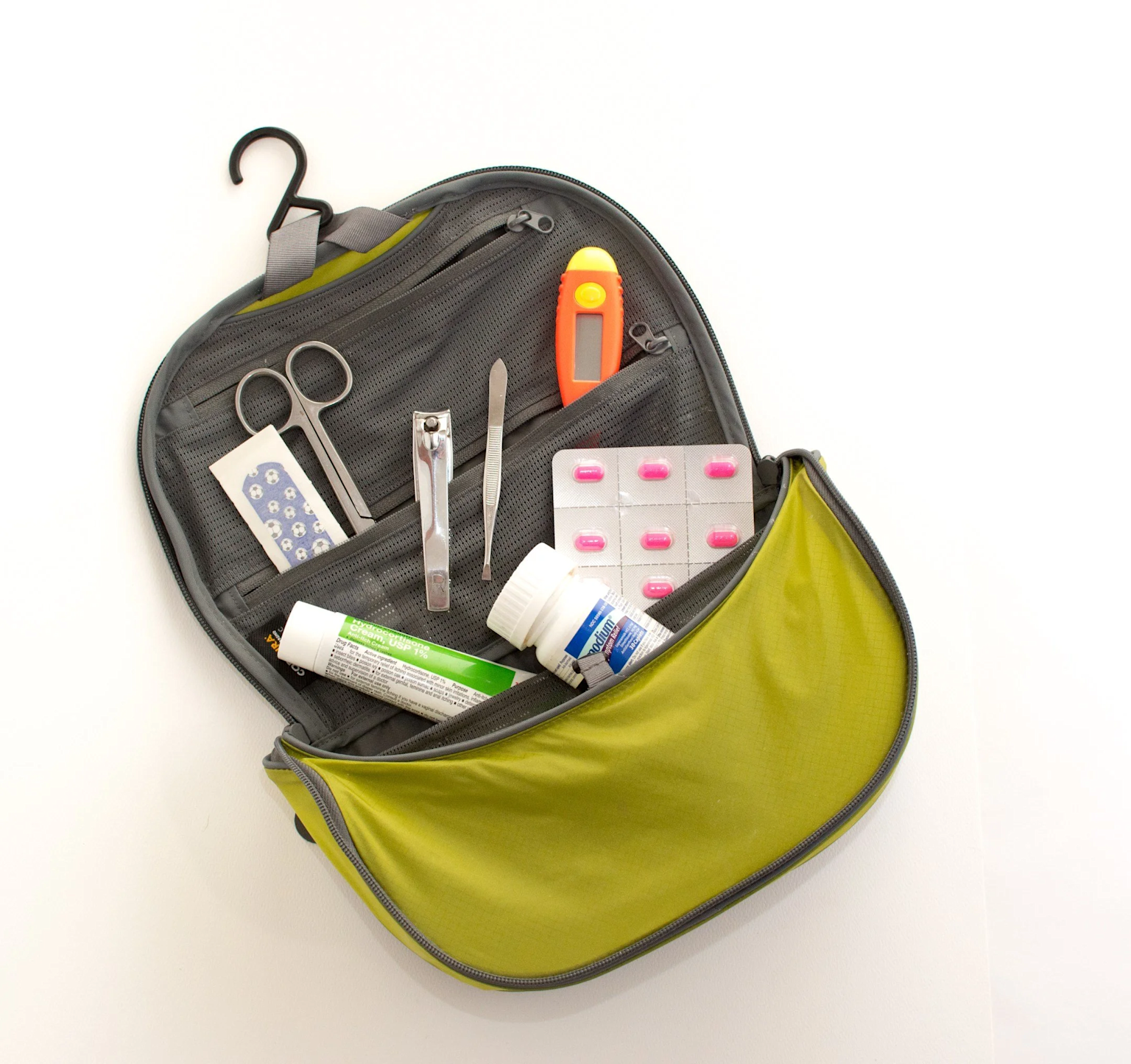 Open toiletry bag with various medical supplies, including pills, a thermometer, and scissors. Green and gray.