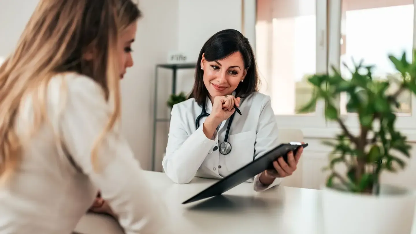 Doctor and patient looking at a clipboard in a medical office, discussing results, with a plant in the foreground.