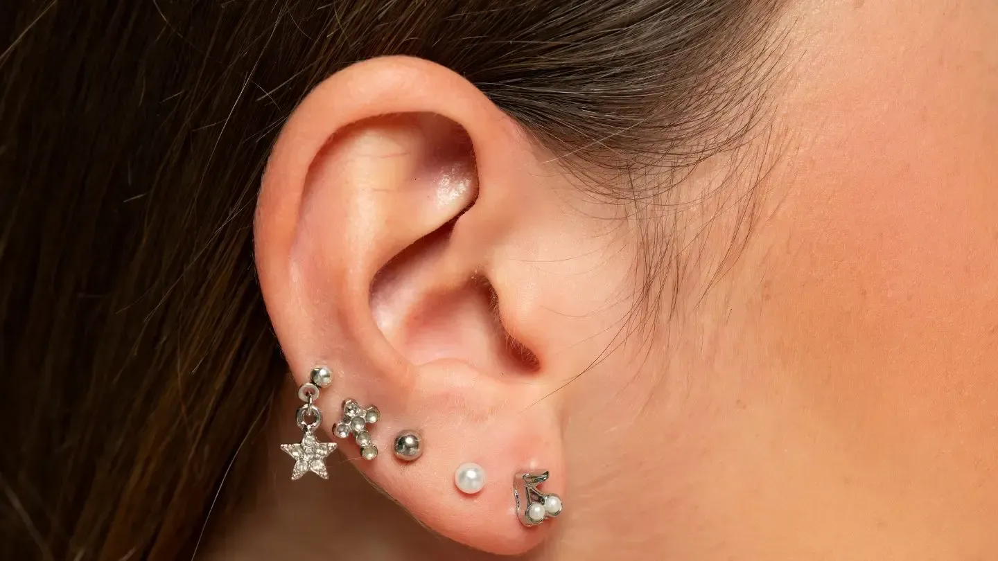 Close-up of an ear with multiple ear piercings, featuring various small, shiny earrings.