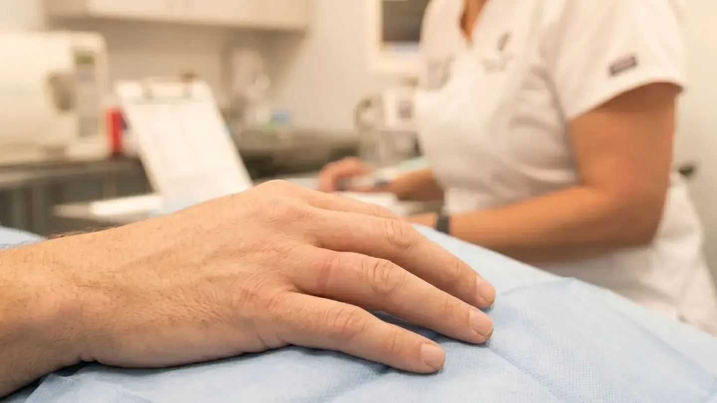 Hand resting on a hospital bed with a clinician blurred in the background