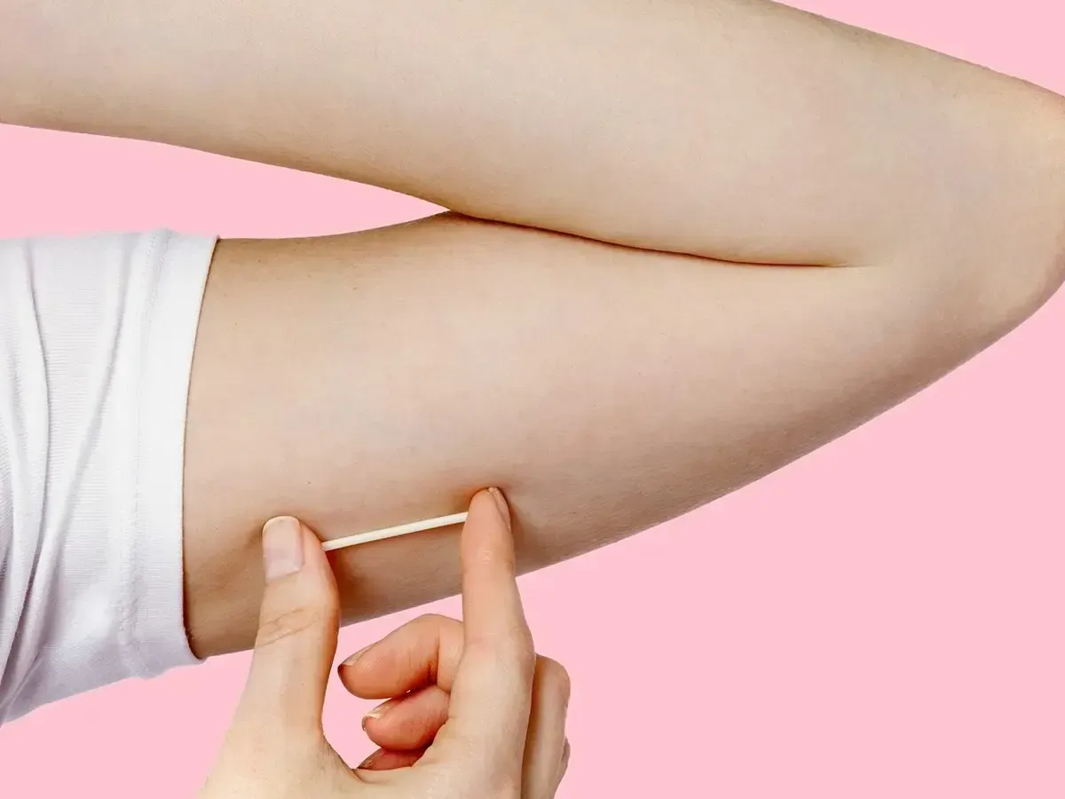 Hand pinching the underside of an upper arm against a pink background
