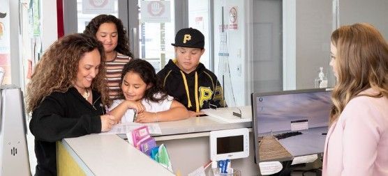 A woman and three children at a reception desk, interacting with a woman. The setting appears to be an office or clinic.