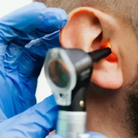 A doctor's gloved hand using an otoscope to examine a person's ear.