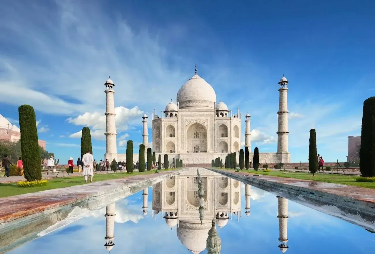 Taj Mahal reflected in a pool of water, under a blue sky.