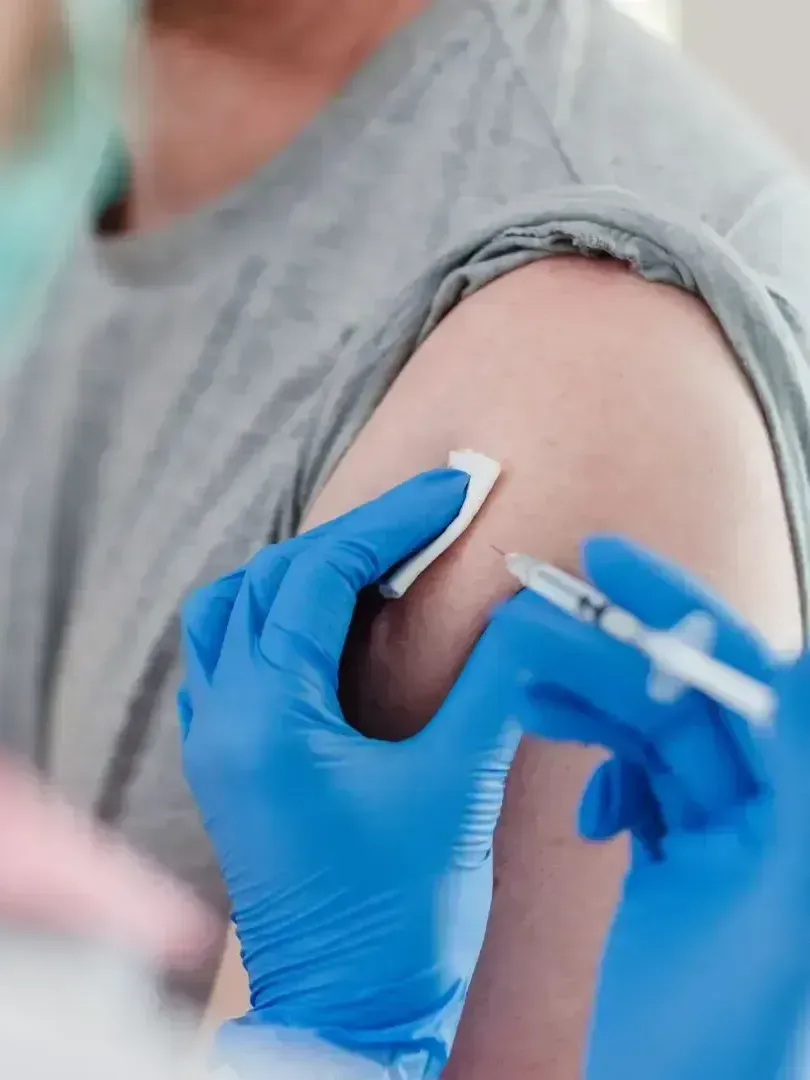 Healthcare worker giving a vaccine shot to a person's upper arm with a blue glove and syringe