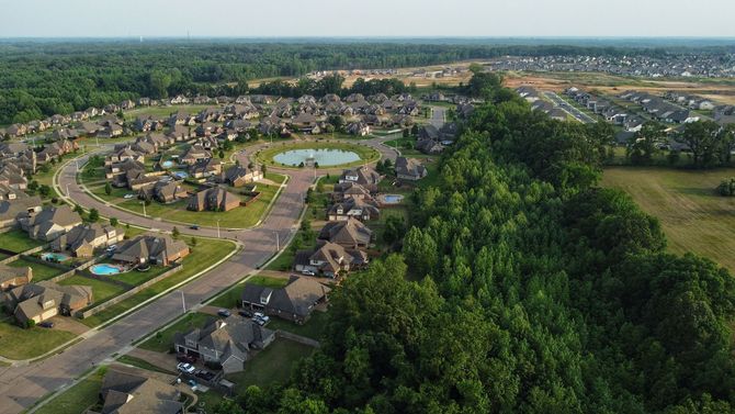 Aerial view of a suburban neighborhood with winding roads, houses, a pond, and trees