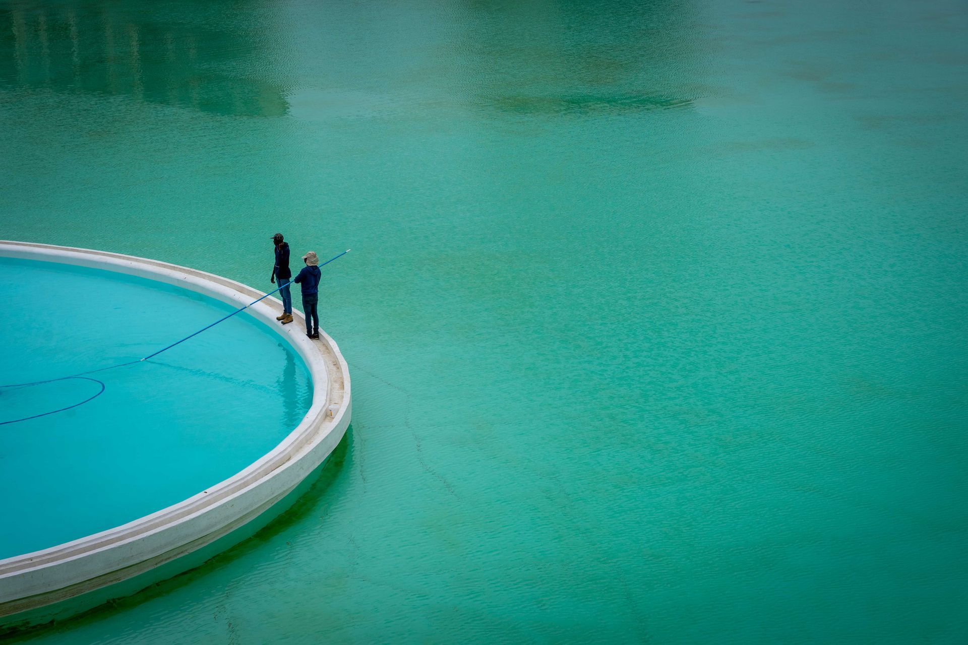 Two people stand by a curved white pool edge beside turquoise water.