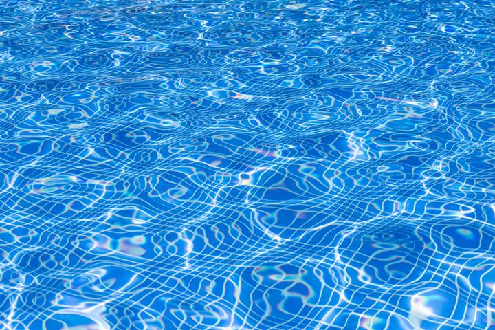 Blue swimming pool water with bright sunlit ripples and reflections