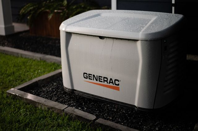 Generator, gray casing, on gravel base, near brick wall. Gas pipes connected.