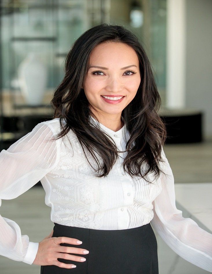 Attorney Quyen - San Diego, CA - Andy Van Lee & Associates, PC Woman in white blouse and black skirt, smiling in modern office setting.