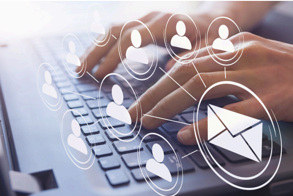 A person is typing on a laptop computer with icons of people and an envelope coming out of the keyboard.