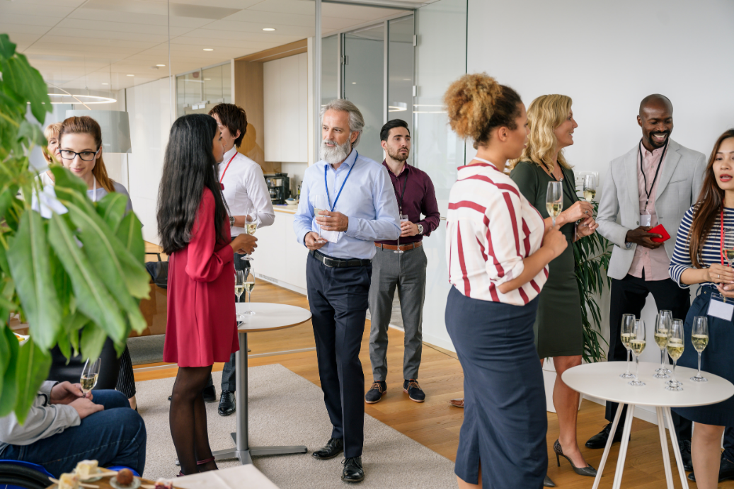 People socializing in a bright office lounge, holding drinks and chatting around a small table.