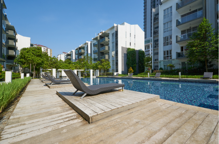Modern apartment courtyard with lounge chairs beside a blue pool and wooden deck under sunny skies