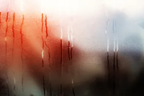Frosted window with red and white streaks, blurred view beyond