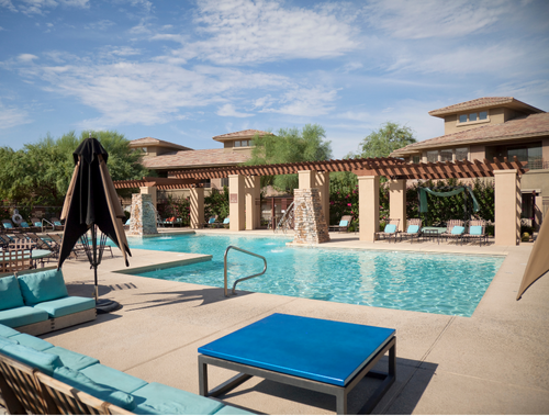 Resort pool with blue water, lounge chairs, pergola, and umbrella under a sunny sky