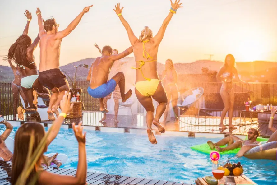 People jumping into a pool at sunset at a lively rooftop party