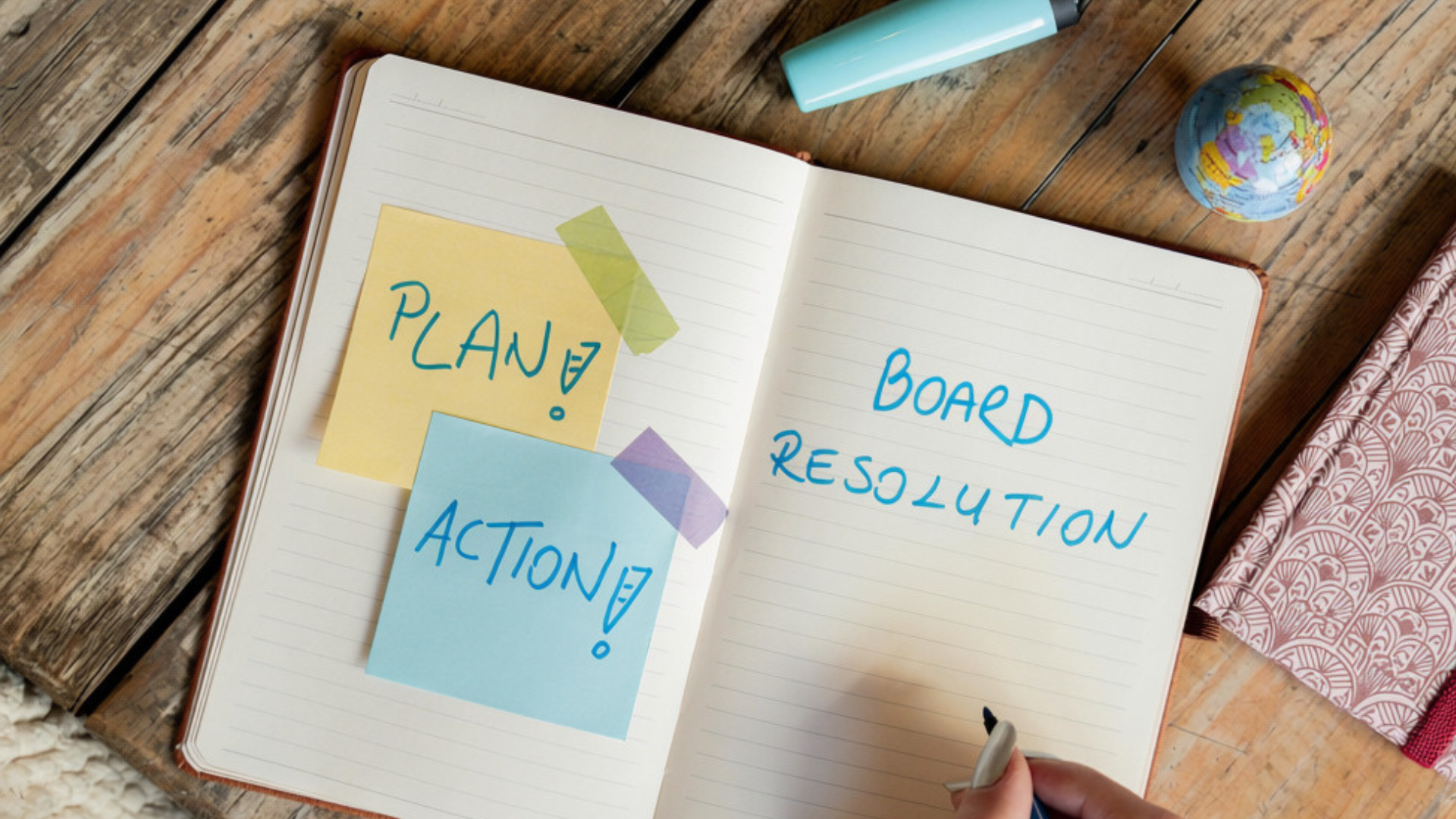 Open notebook with sticky notes reading “Plan?” and “Action!” beside “Board Resolution” on a wooden desk