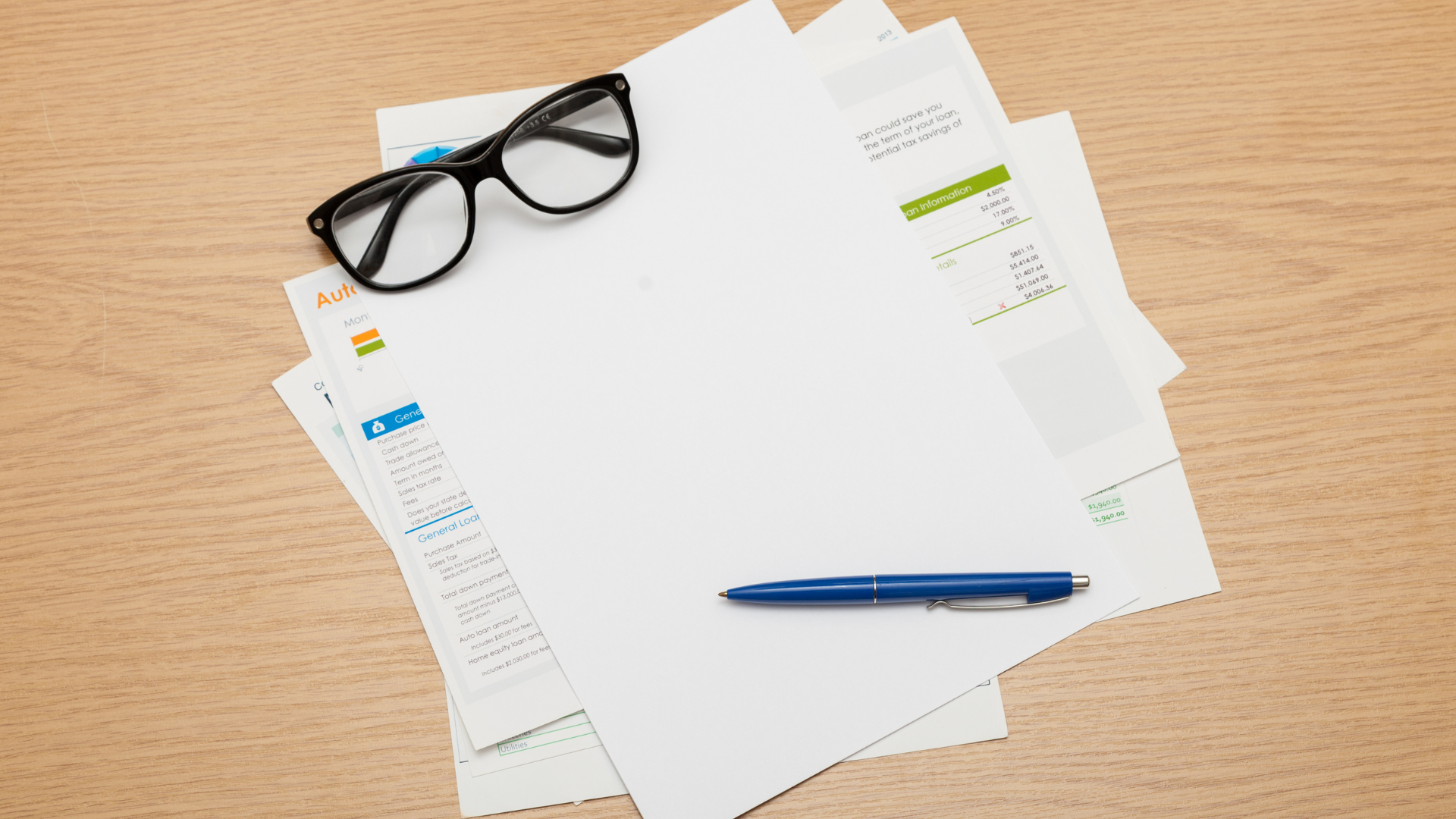 Glasses, pen, and paperwork spread on a wooden desk