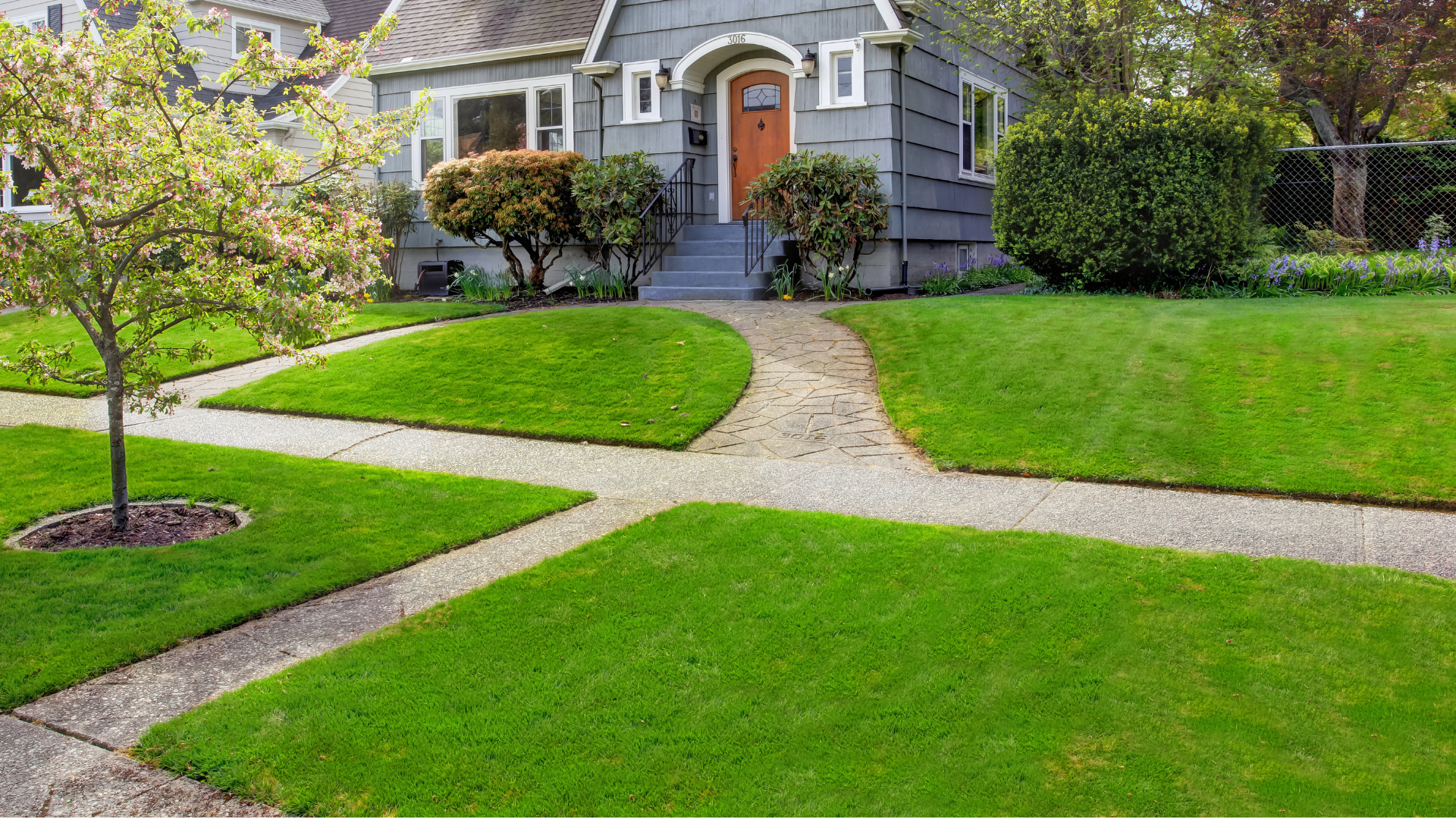 Curved walkway across a green front lawn leading to a gray house with a brick arched doorway.