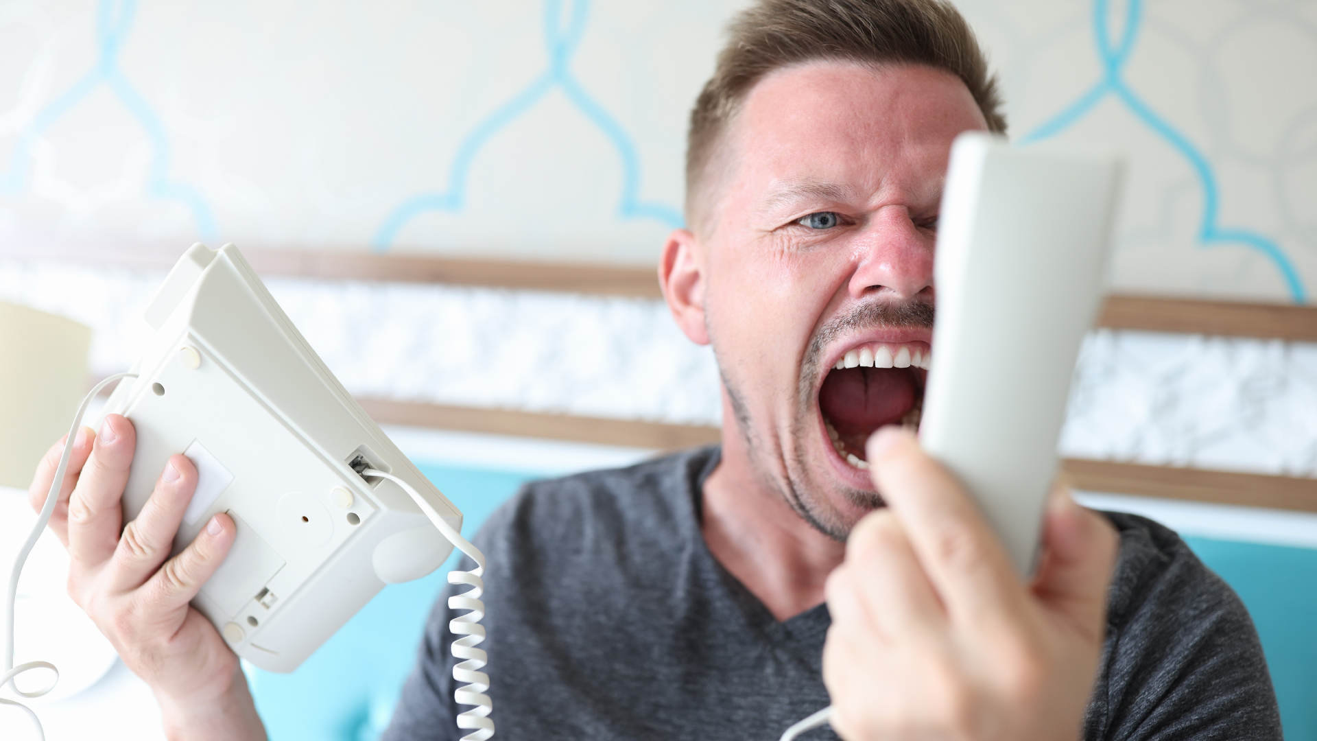Angry man yelling while holding two white landline phone handsets indoors