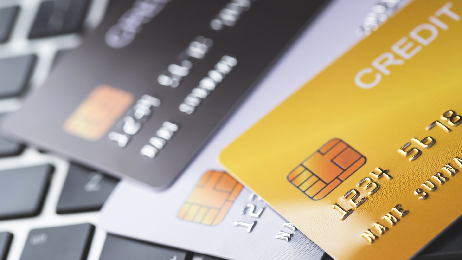 Credit cards on a laptop keyboard, one gold card in the foreground