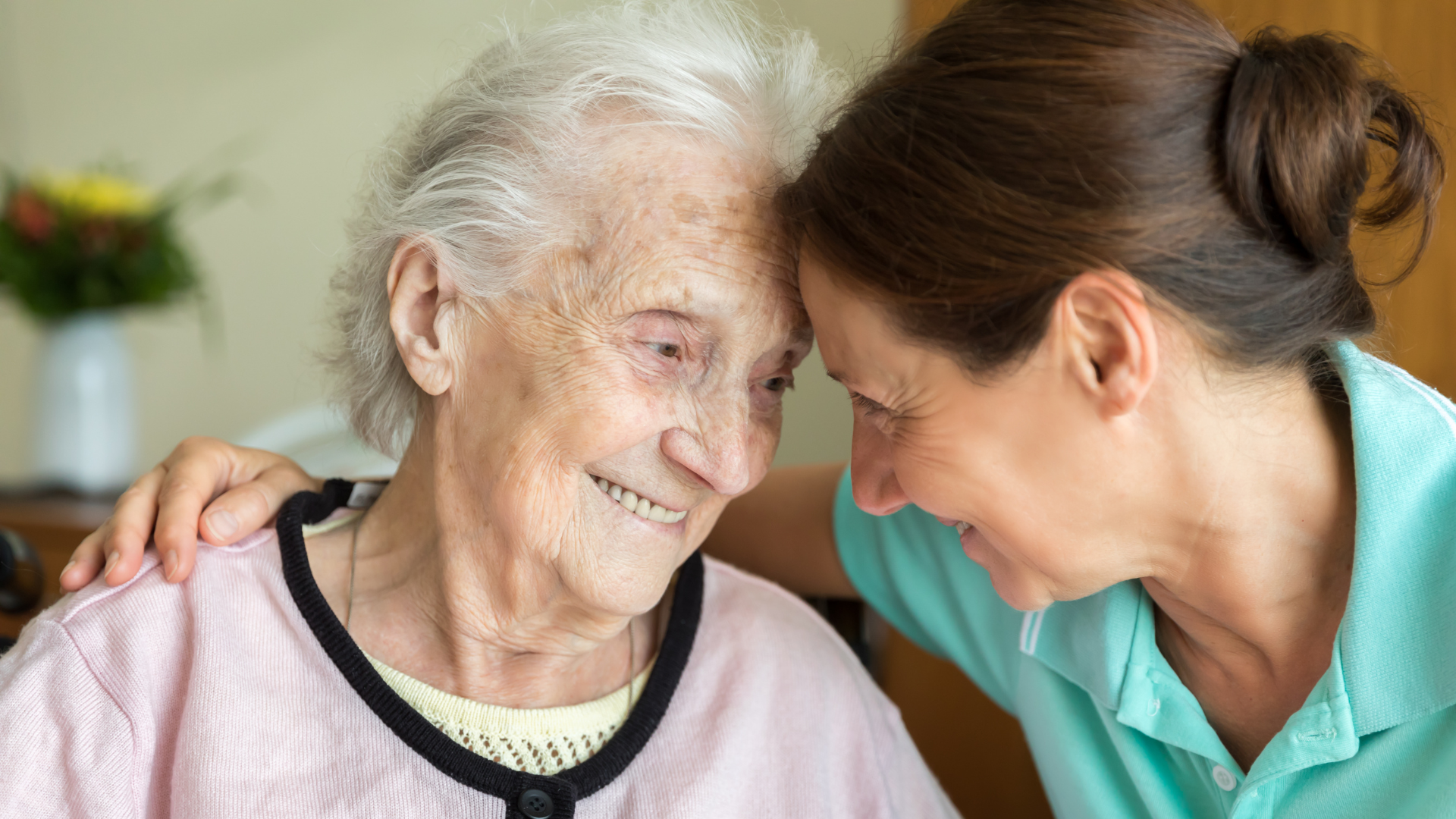 Two people smiling and leaning close in a warm, caring moment indoors