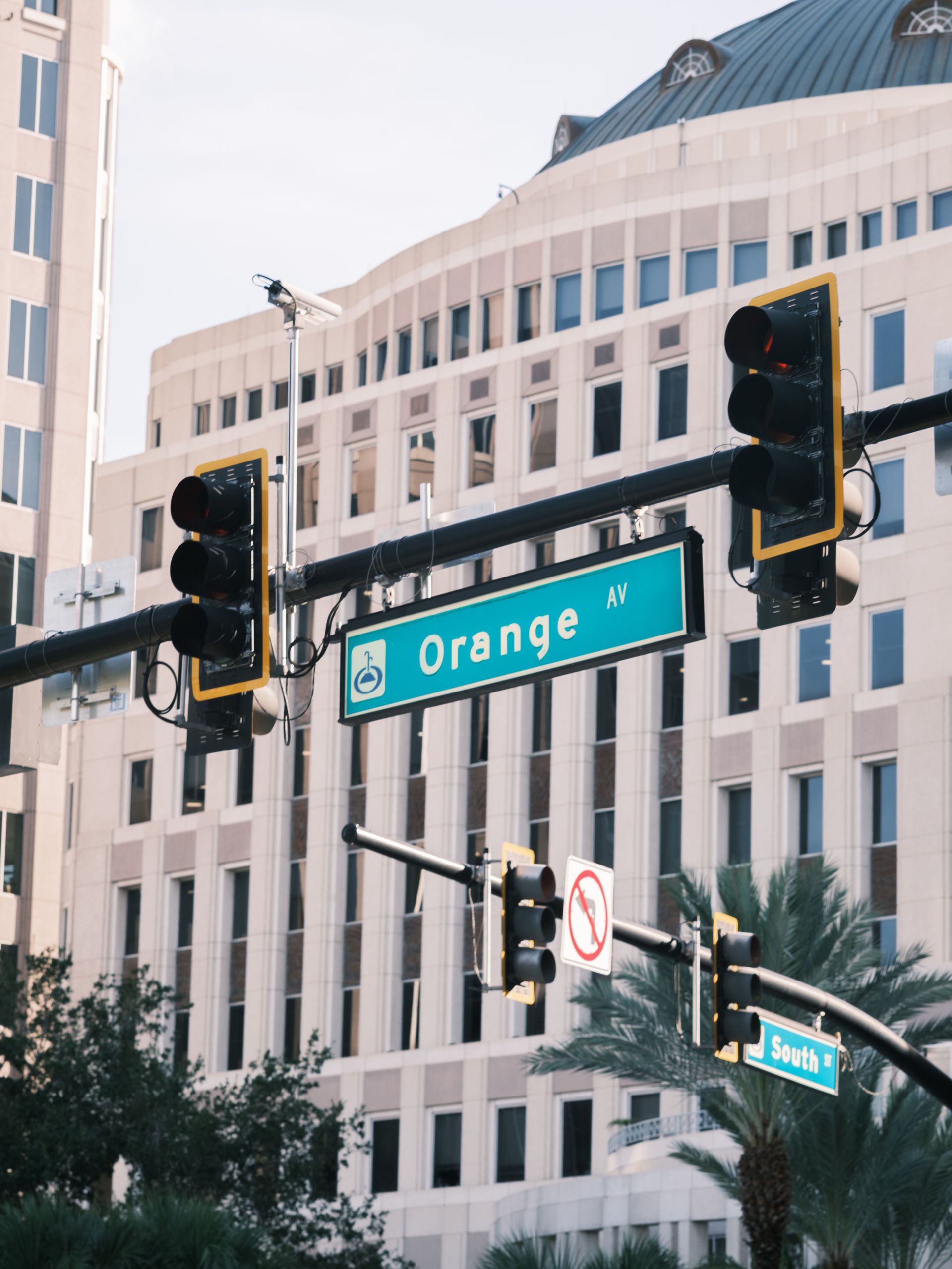 Street signs and traffic lights at an intersection beside a large white building, including an orange avenue sign.