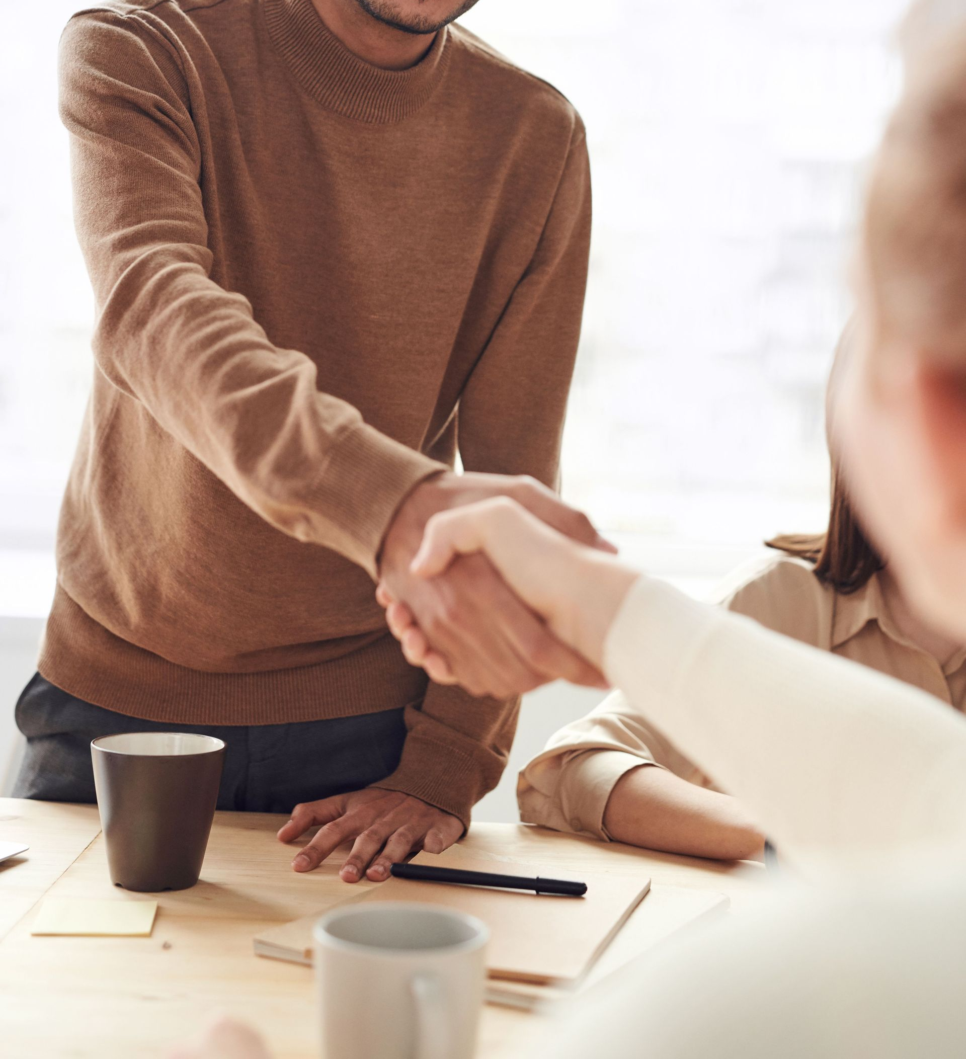 Two men in a bright office shake hands and smile across a table