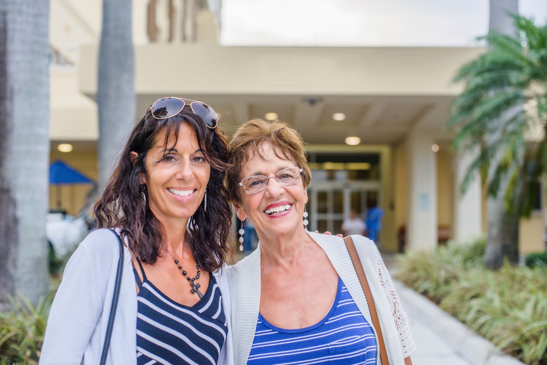 Two smiling women standing in a bright indoor lobby, wearing striped tops.