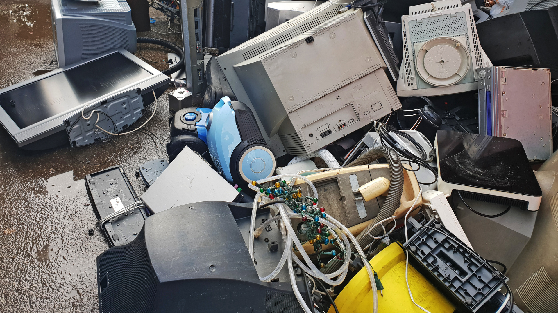Pile of discarded electronics and scrap metal scattered on a wet surface outdoors