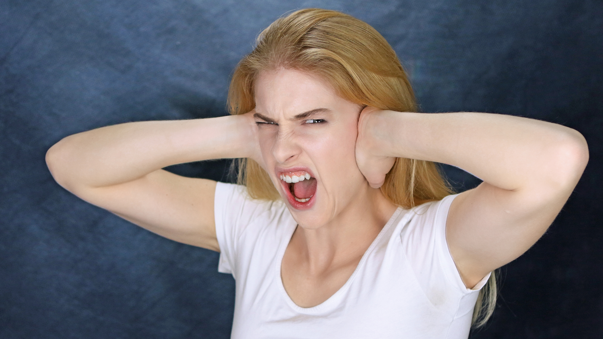 Woman covering her ears and shouting against a dark blue background.