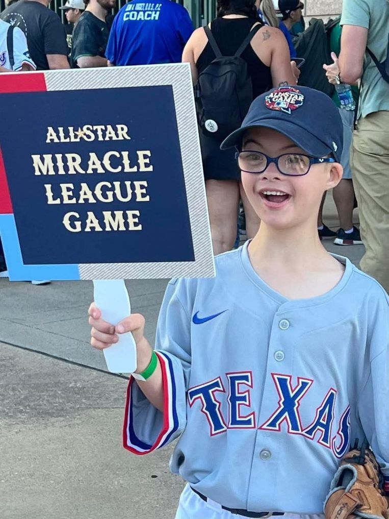 A boy in a texas jersey is holding a sign for the all star miracle league game