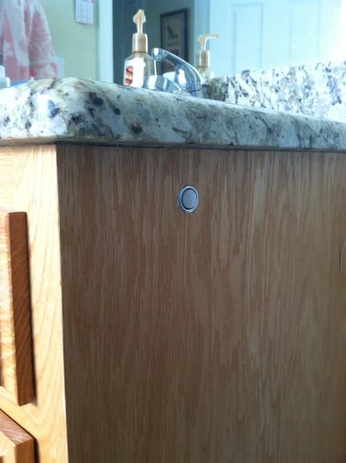 Close-up of a wooden cabinet with a small circular push-to-open latch beneath a speckled countertop.