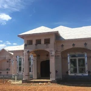 House under construction on a sunny day; light-colored exterior, covered windows, blue sky.