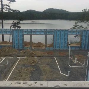 Construction site with blue insulated concrete form walls, lake, and mountains in background.