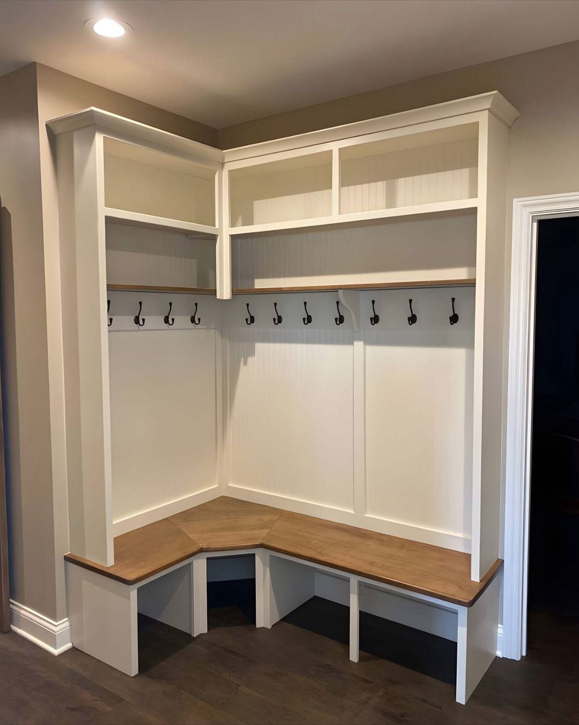 Built-in corner mudroom bench and coat hooks with white cabinets and wood seat