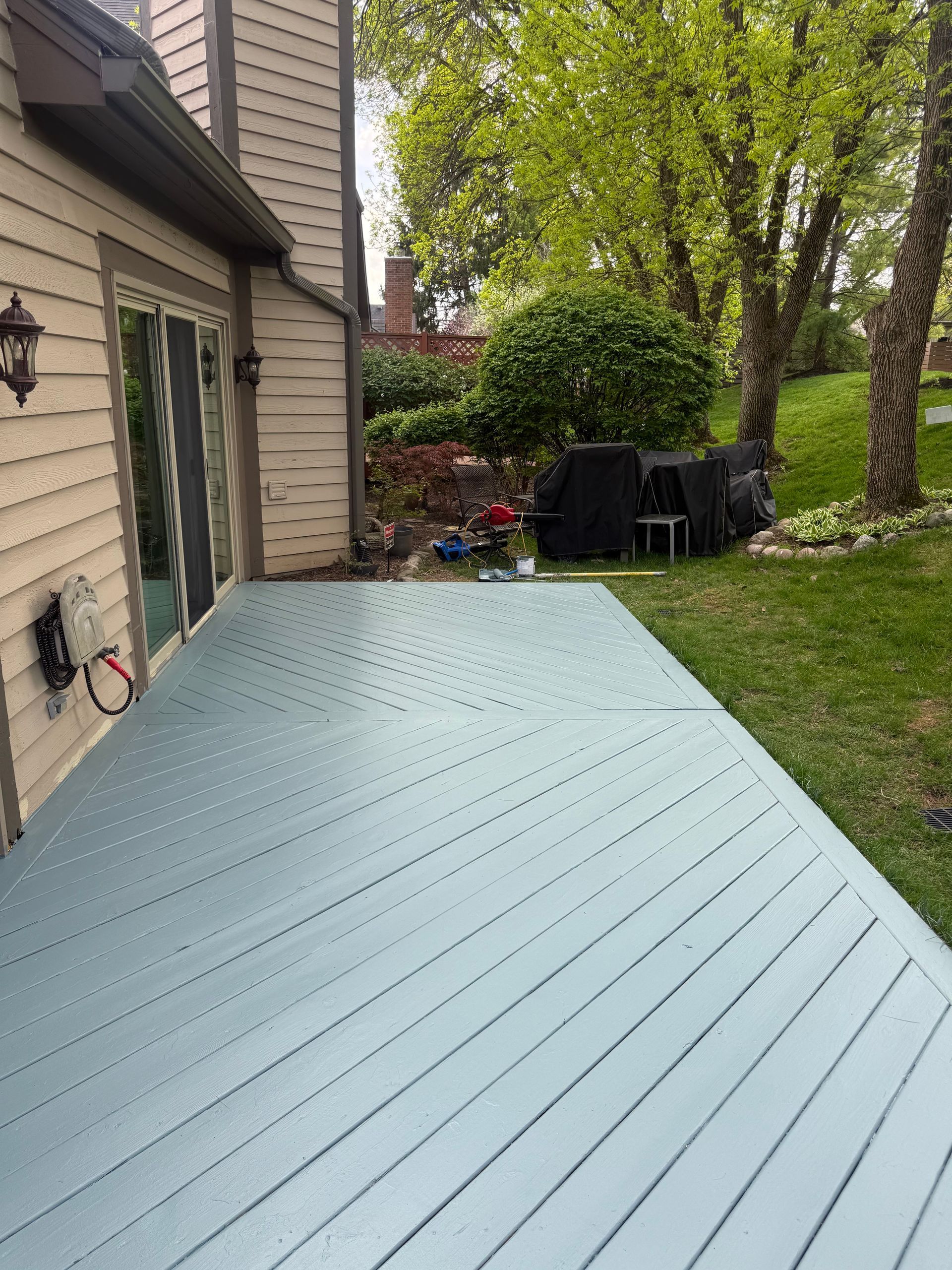 Light blue deck beside a house, with trees and a grassy yard in the background.