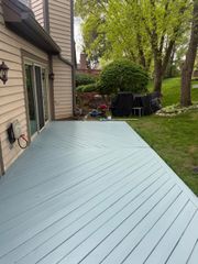 Light blue deck beside a house, bordered by grass and trees in a backyard.
