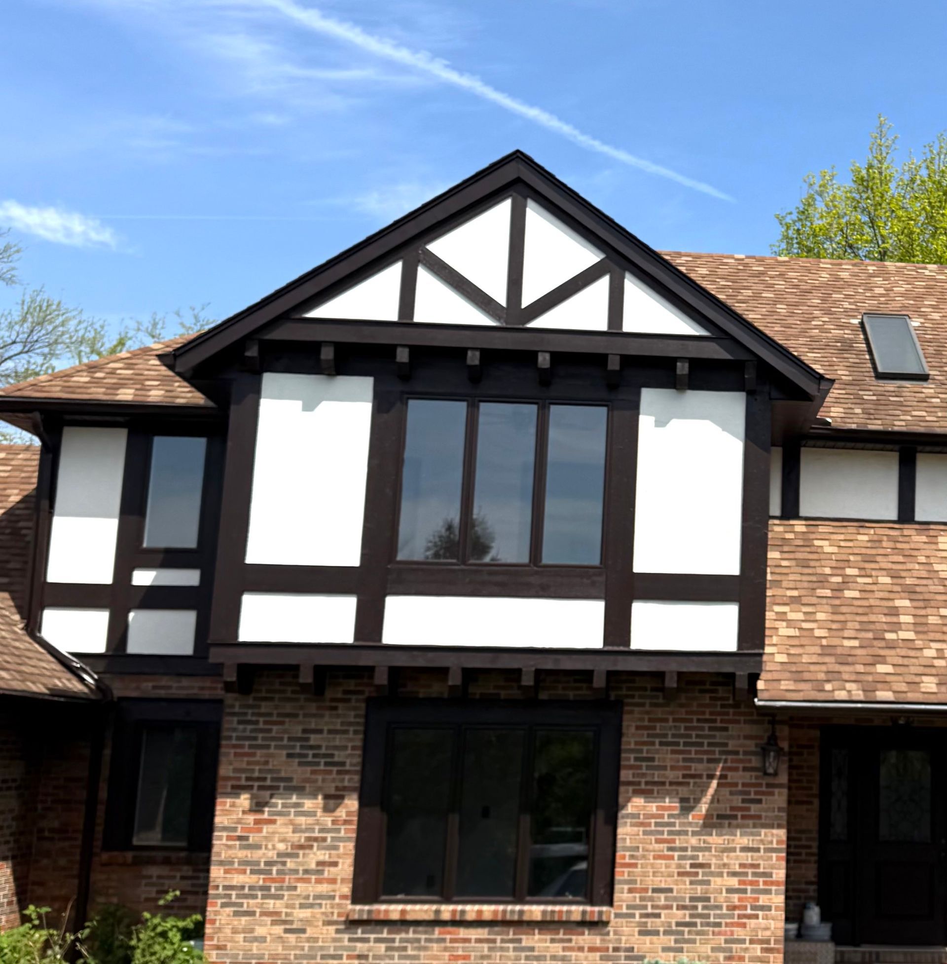 Brick Tudor-style townhouse with white and black trim and large windows under a blue sky