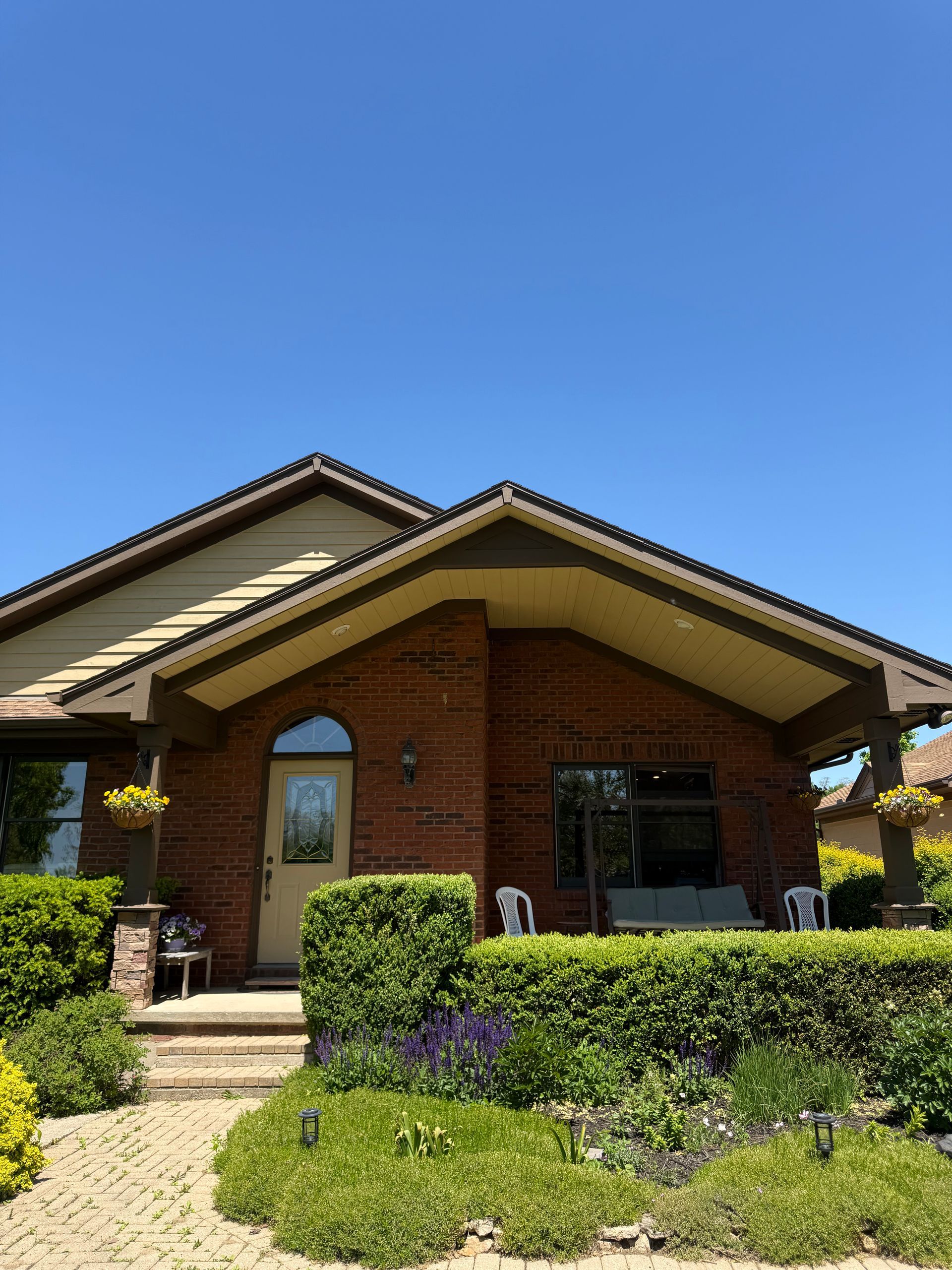 Brick house with a covered porch, landscaped front yard, and clear blue sky.