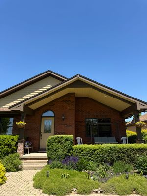 Brick house with a covered porch, green shrubs, and a clear blue sky.