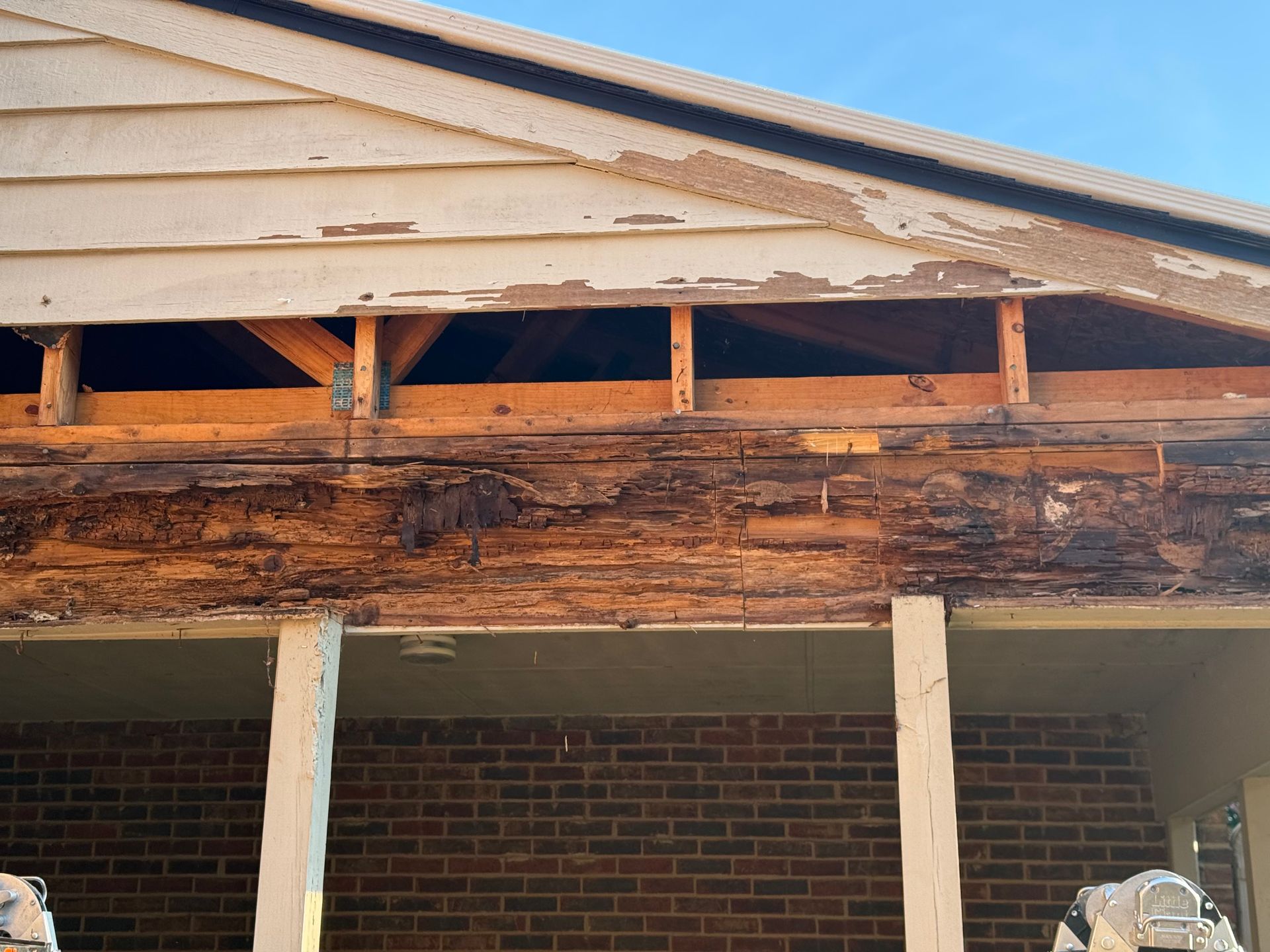 Severely weathered wooden beam under a house roof, with exposed framing and brick wall below