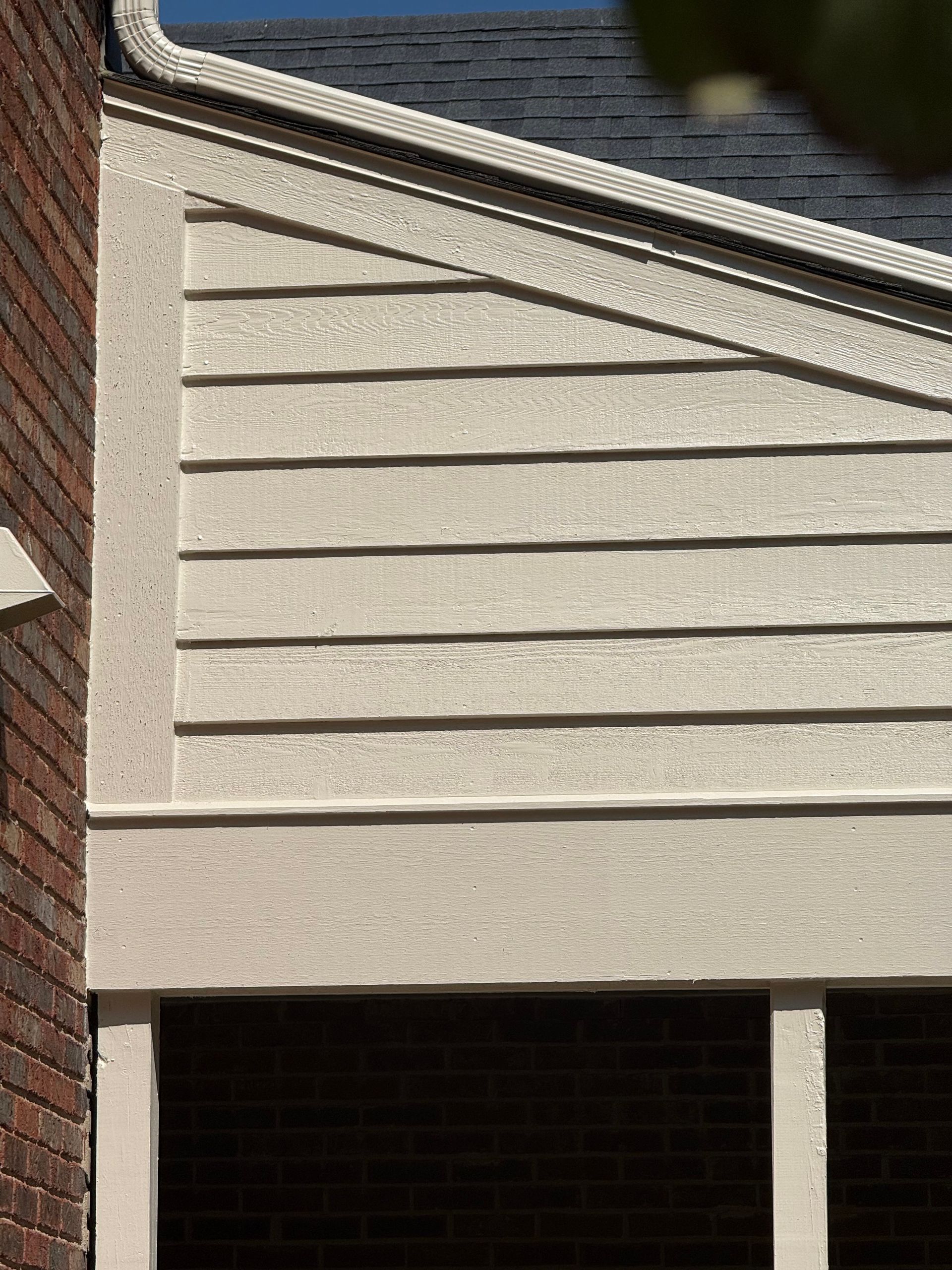 Exterior of a house with beige siding, brick wall, and a garage opening underneath
