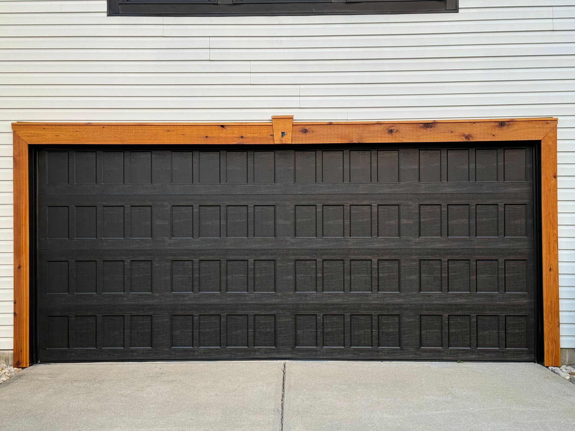 Black garage door with wood trim on a white house exterior