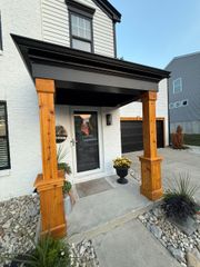 Front porch with wooden posts, gray siding, white brick, and potted flowers beside a stone walkway.