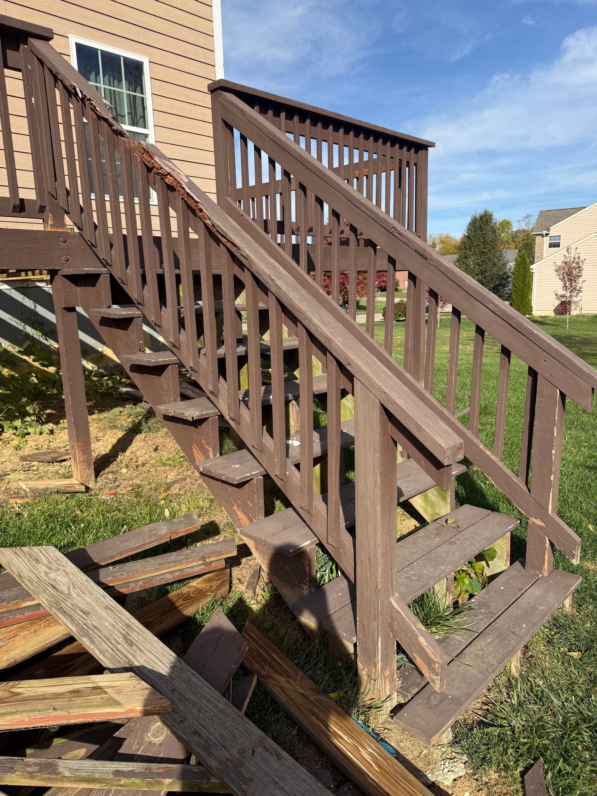 Weathered wooden exterior staircase beside a brick building, with railings and steps over grass.