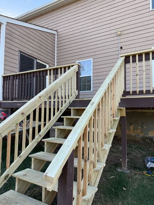 Wooden outdoor stairs leading to a raised deck beside a beige house with blue shutters