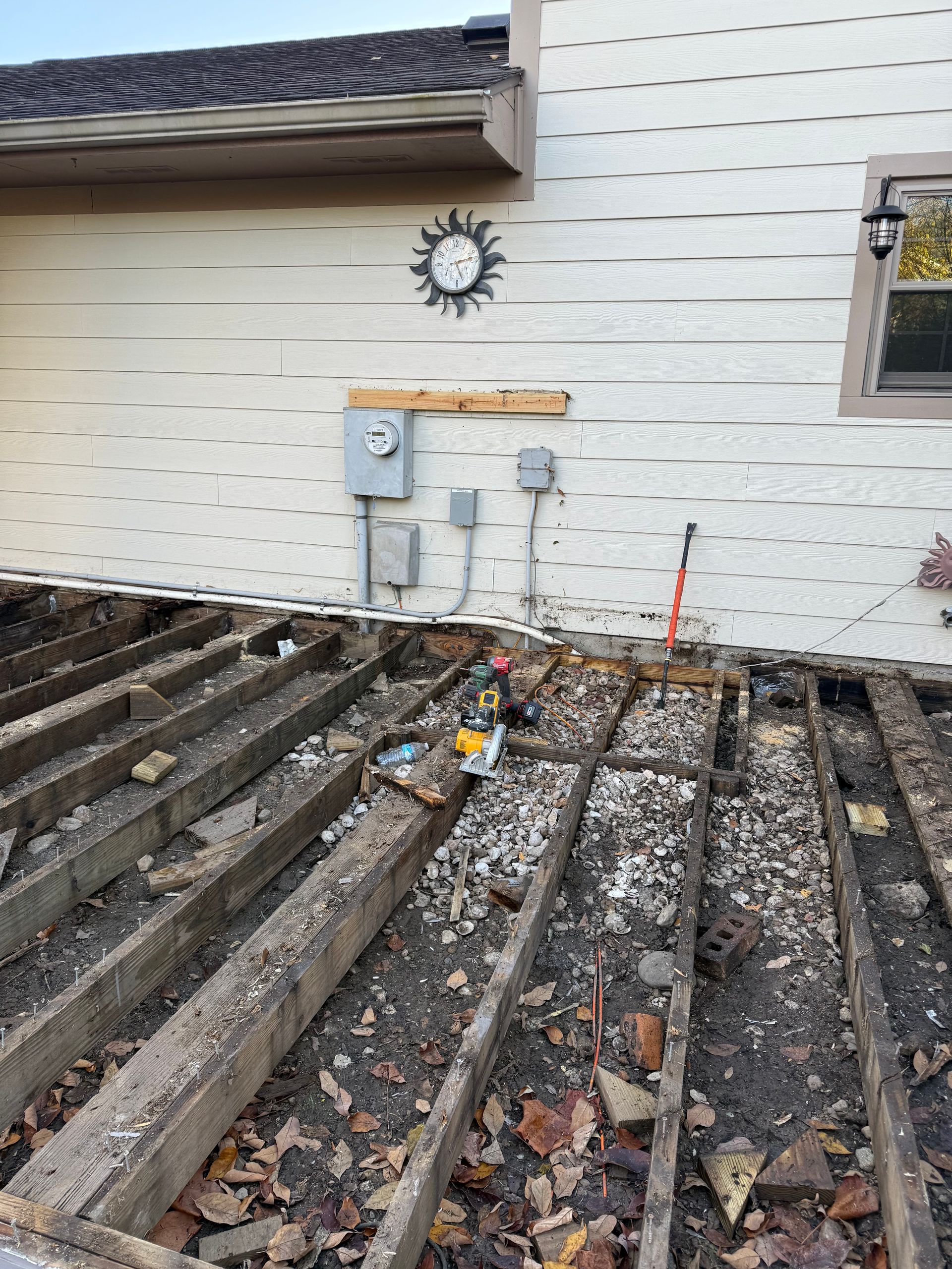 Damaged wooden deck beside a white house with exposed ground and utility meters on the wall