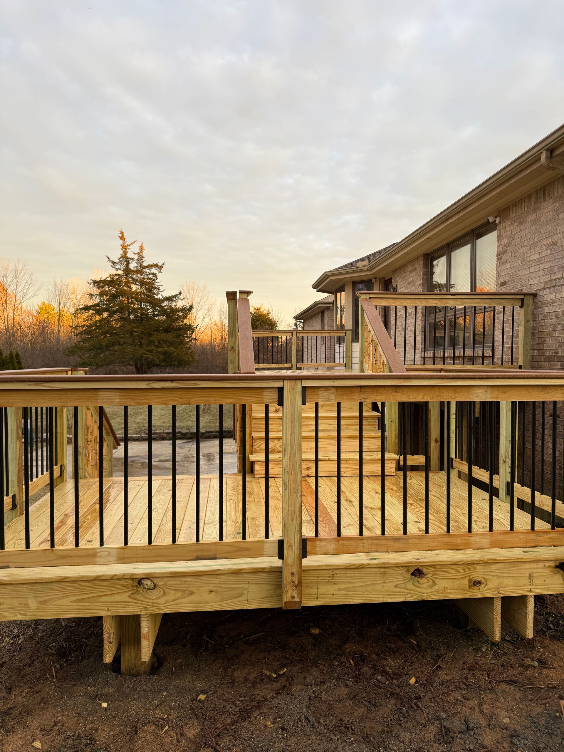 Wooden deck and railing outside a house at sunset with trees in the background