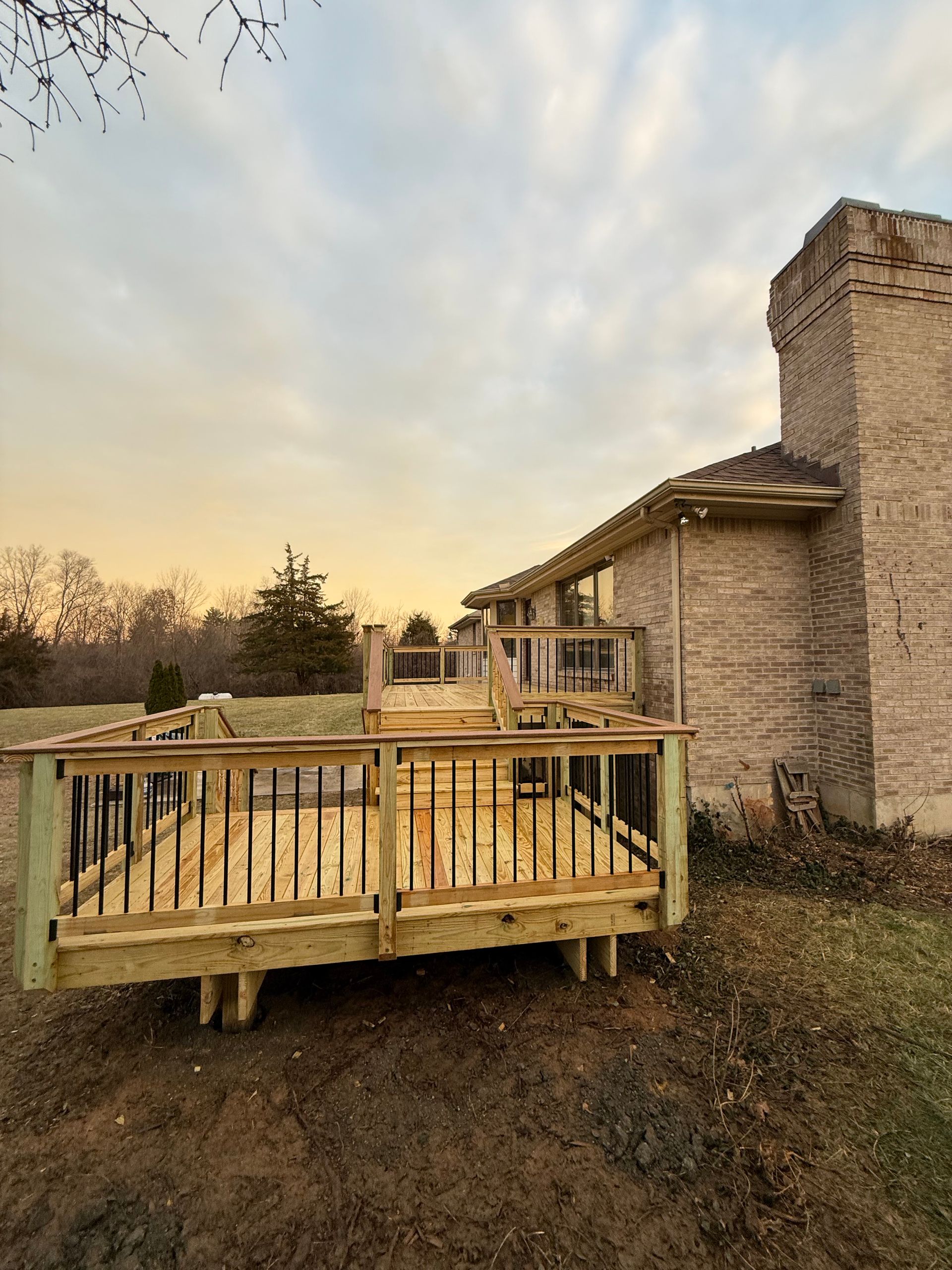Wooden deck and stone house at sunset with a fenced yard and cloudy sky
